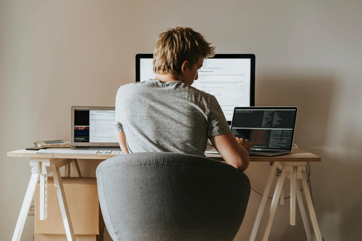 Person working at desk with multiple screens experiencing work-related stress and sedentary lifestyle challenges