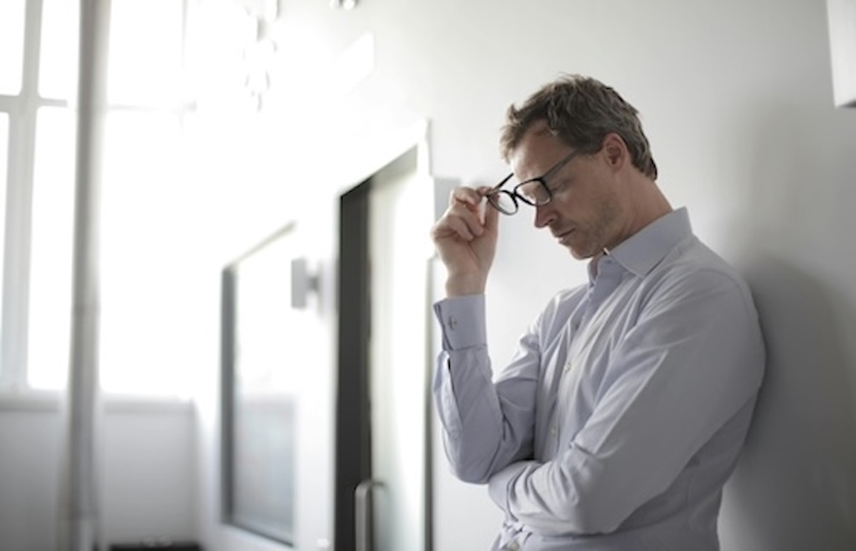 Man in office setting touching glasses showing signs of stress, eye strain, and mental fatigue at work to illustrate reflections about understanding your emotions