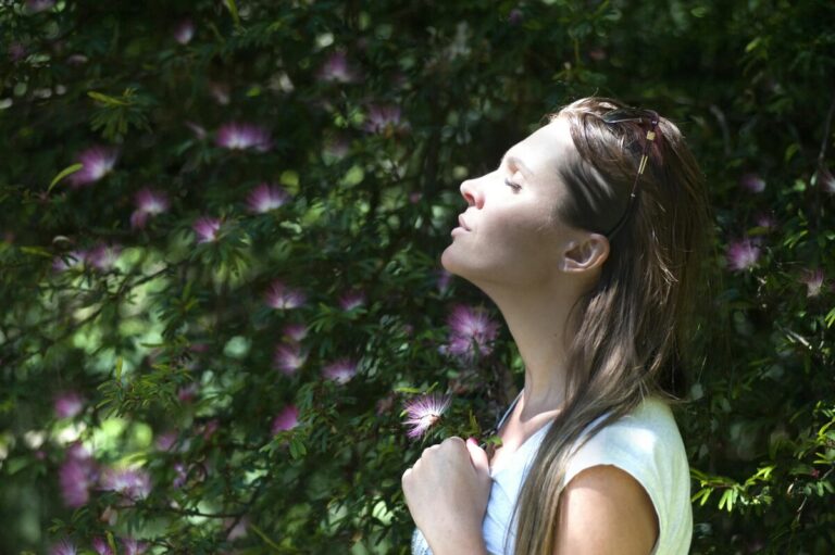 Woman practicing deep breathing outdoors in nature with eyes closed, surrounded by purple flowers