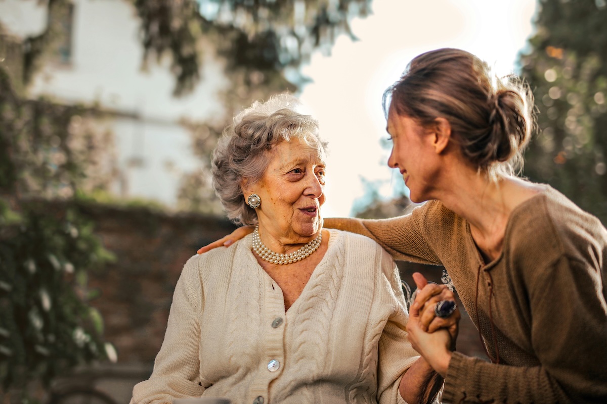Elderly woman and younger woman sharing a warm moment outdoors, representing healthy aging and longevity through stress management and wellness practices